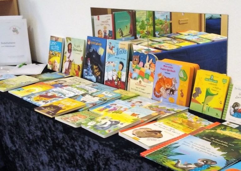 Büchertisch Bunte Kinderbücher auf einem Tisch mit blauer Tischdecke, verschiedene Buchtitel und Illustrationen, nach Themen sortiert.